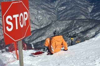Snowboarder rutschend im Hang hinter dem Stopp-Schild